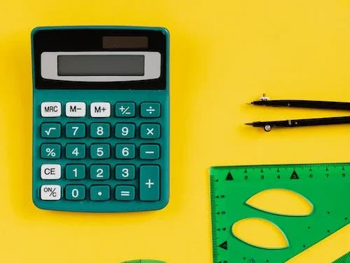 Calculadora e régua de cor verde e compasso preto em fundo amarelo.